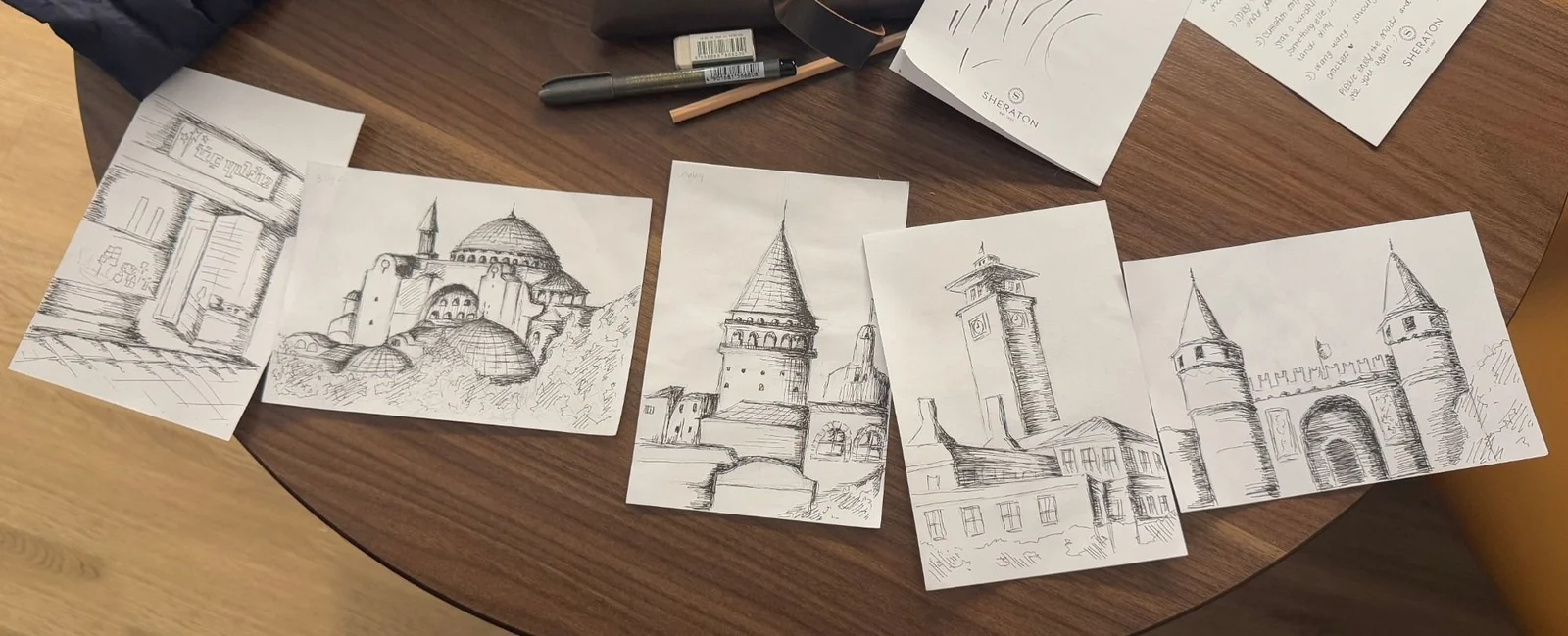 Five pen sketches of Istanbul landmarks laid out on a wooden table